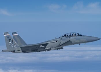 An F-15EX fighter jet against a blue sky.