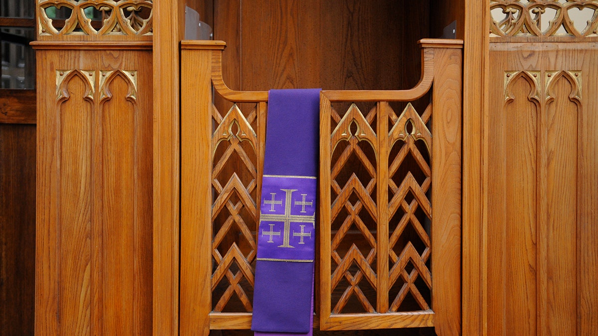 A purple stole with a Jerusalem cross hangs over a confessional