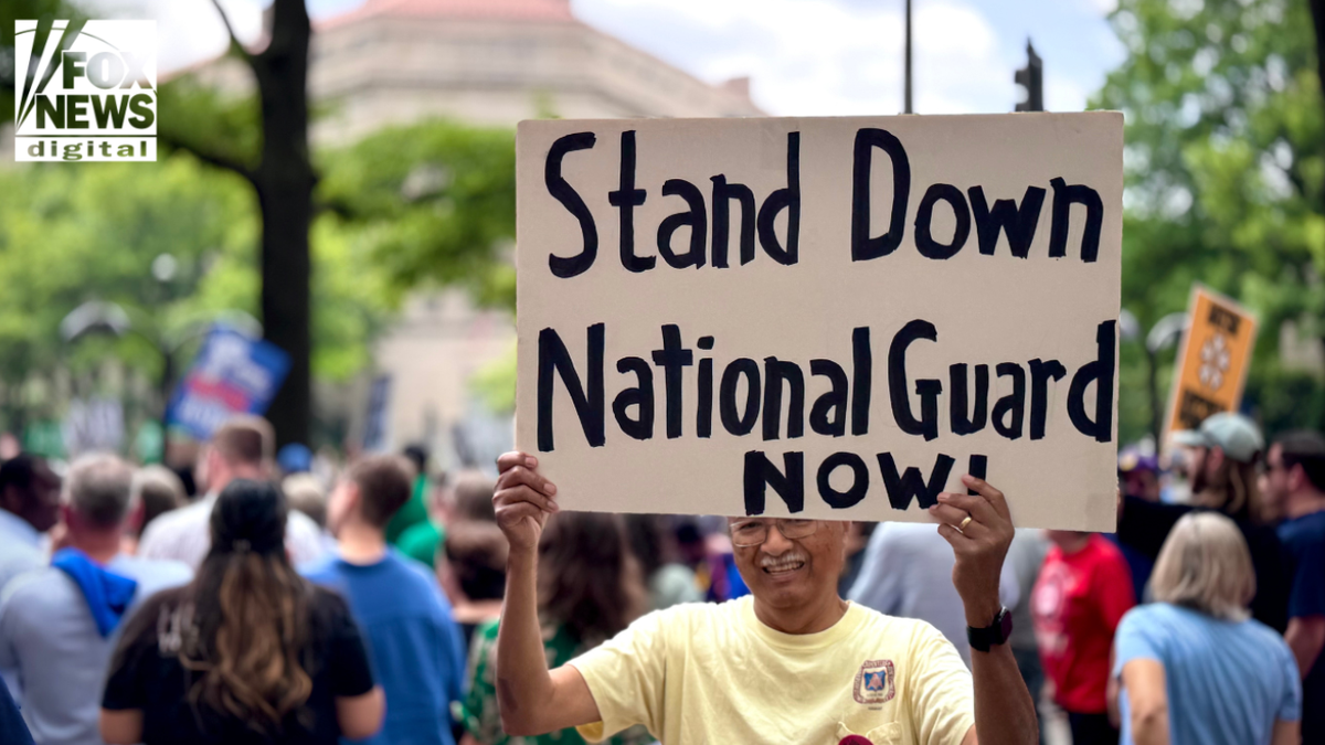 A protester in a yellow shirt holds a large sign reading