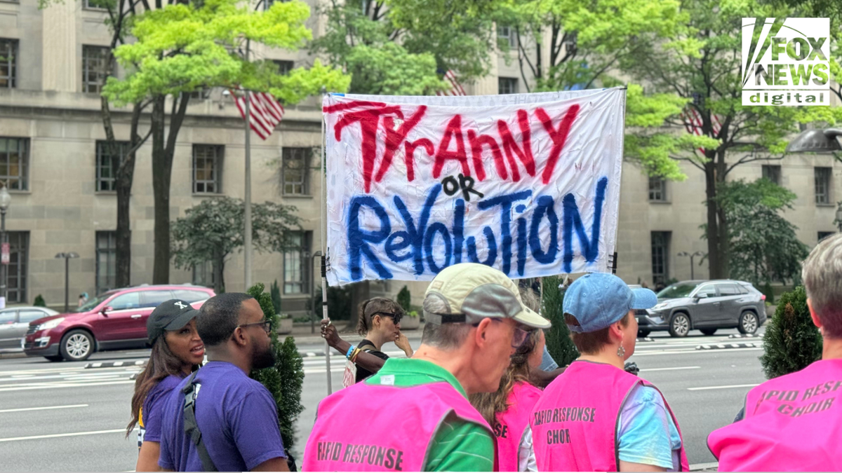 Protesters march outside a federal building in Washington, D.C., holding a banner that reads "Tyranny or Revolution" during a political demonstration. Some wear pink "Rapid Response Choir" vests.