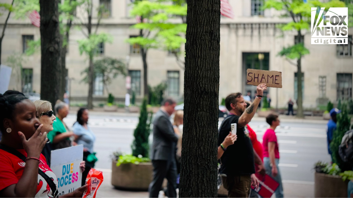 A protester raises a cardboard sign reading