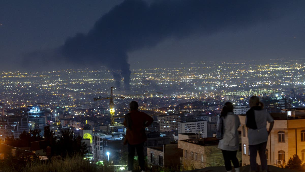 People gather on a hill to watch smoke rising in the distance from an Israeli airstrike in Tehran, Iran, on June 14, 2025.