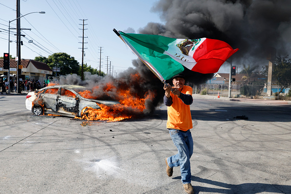 Anti-ICE protesters celebrate in front of a burning car in Los Angeles