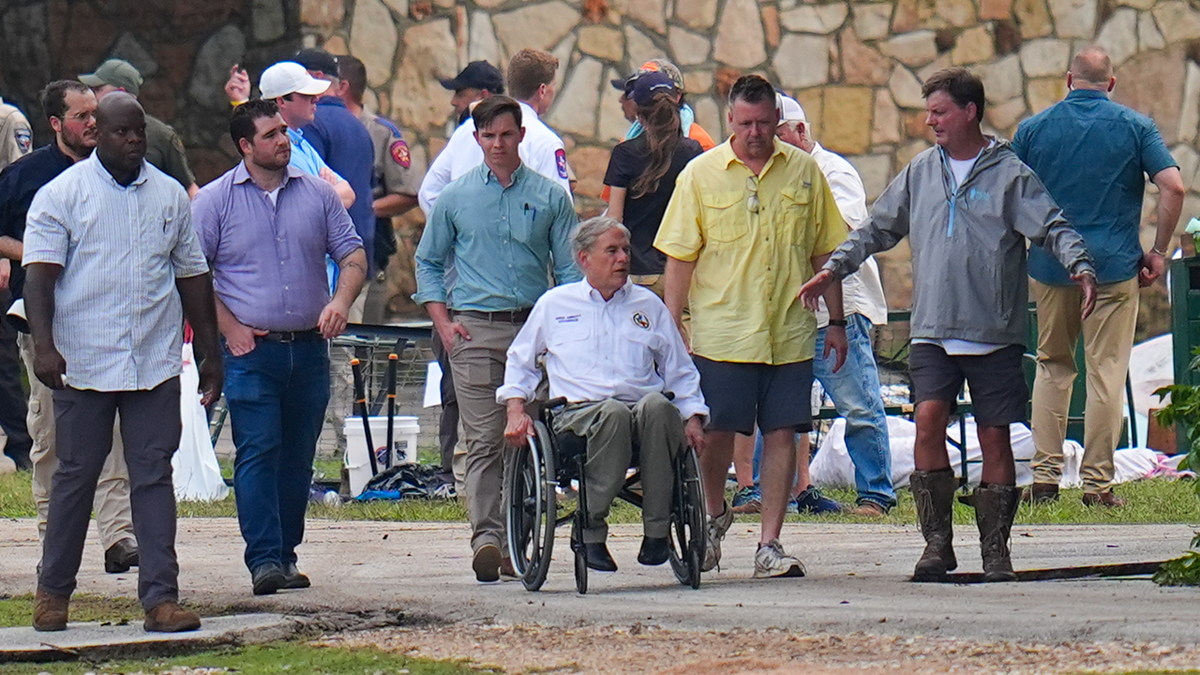 Texas Gov. Greg Abbott, center, tours Camp Mystic along the banks of the Guadalupe River after a flash flood swept through the area Saturday, July 5, 2025, in Hunt, Texas.