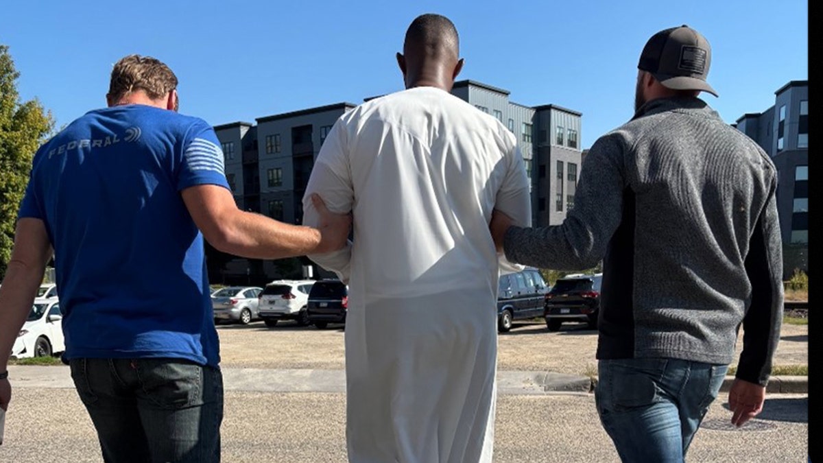 USCIS officers walk alongside a detained immigrant