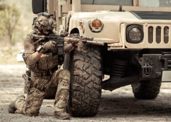 A soldier kneeling behind an armored vehicle.