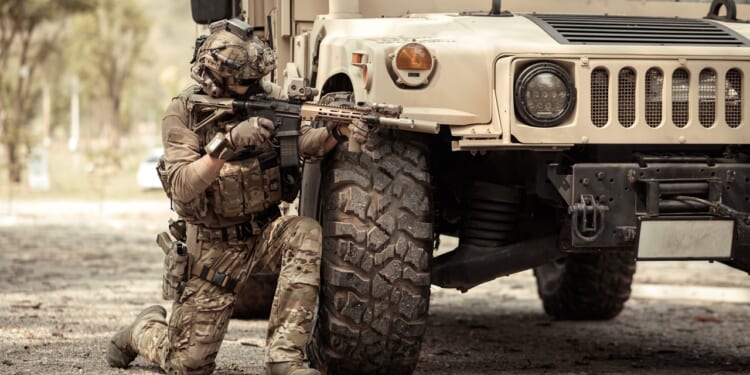 A soldier kneeling behind an armored vehicle.