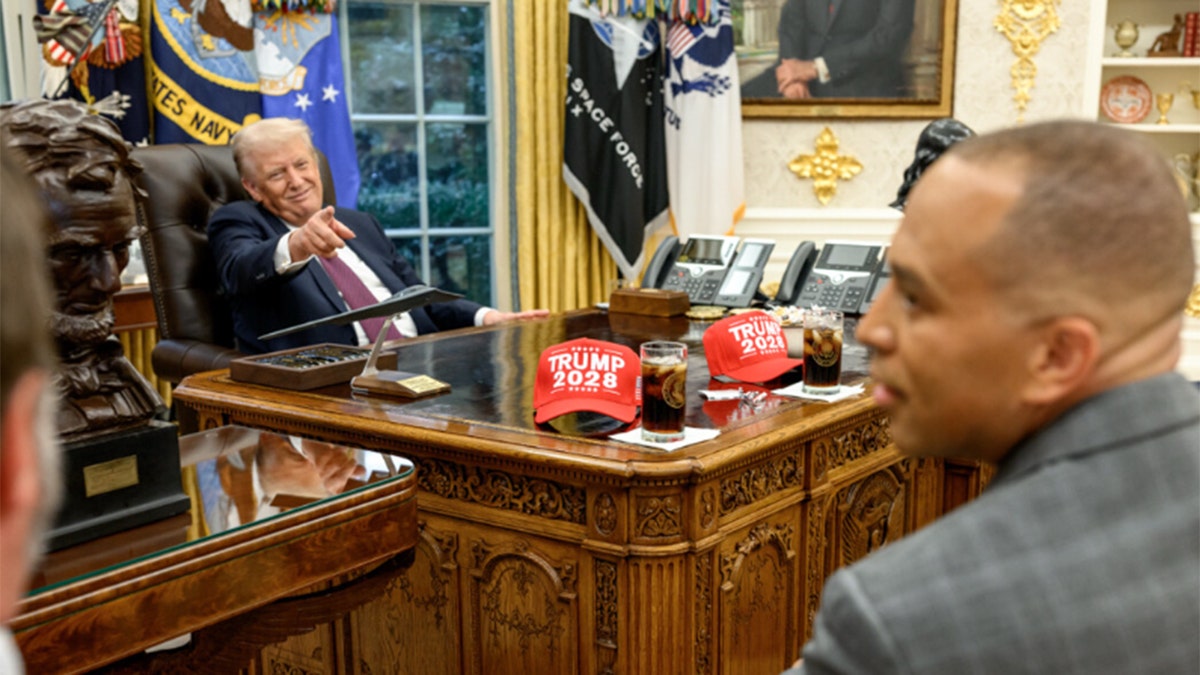 Trump points across Oval Office desk with Trump 2028 hats displayed
