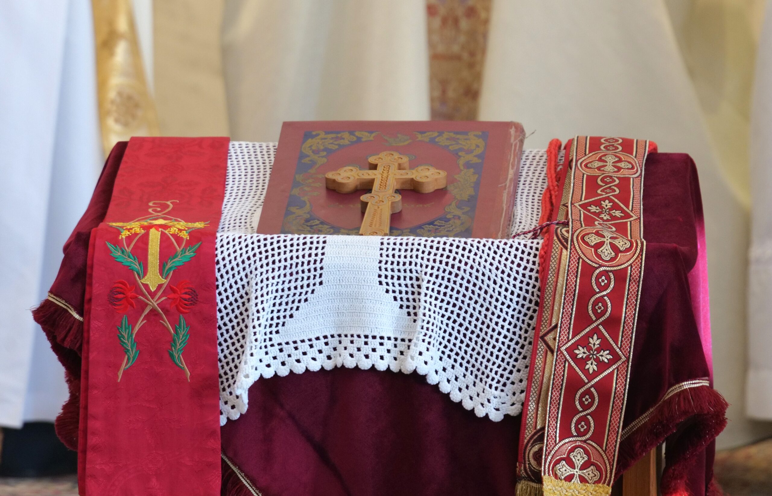 Wooden cross on a decorative altar cloth with embroidered red and white elements, symbolizing a religious setting.
