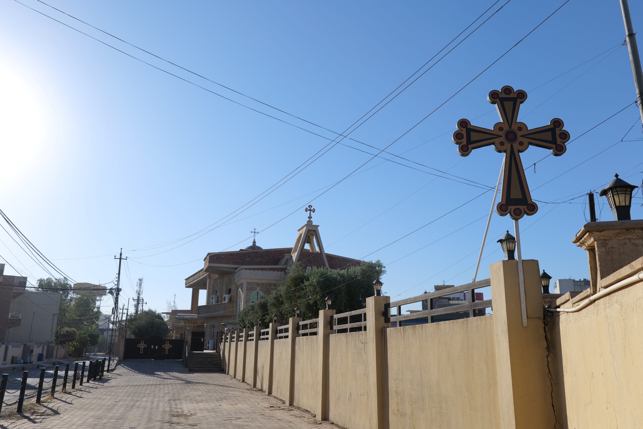 Street view of a building with a cross and surrounding power lines under a clear blue sky.
