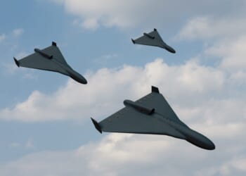 Group attack of black drones of modern suicide bombers flying against the background of blue sky and clouds.