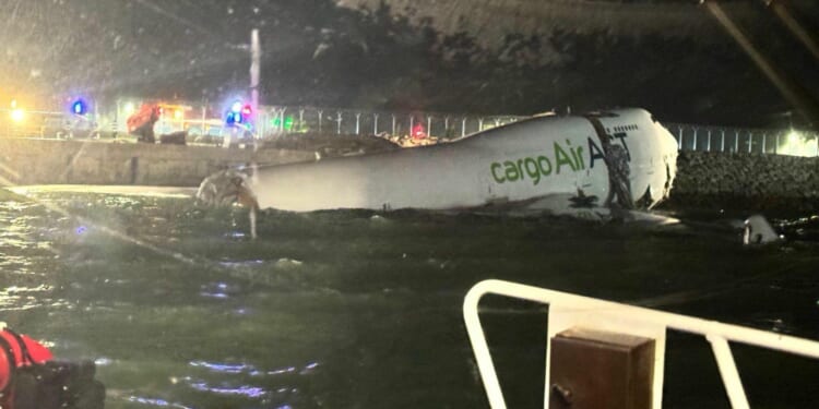 CargoAir aircraft partially submerged in water at night with emergency vehicles and lights in the background, indicating a potential aviation incident.