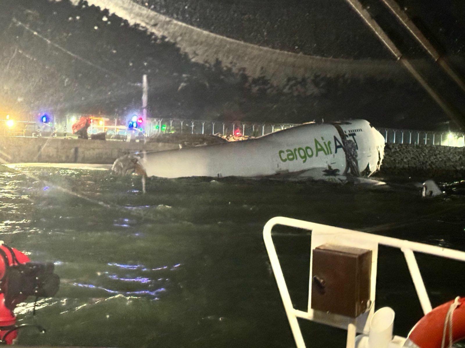 CargoAir aircraft partially submerged in water at night with emergency vehicles and lights in the background, indicating a potential aviation incident.
