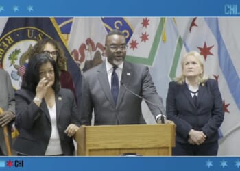 Press conference featuring Chicago officials discussing community initiatives, with multiple flags in the background and speakers at a podium.