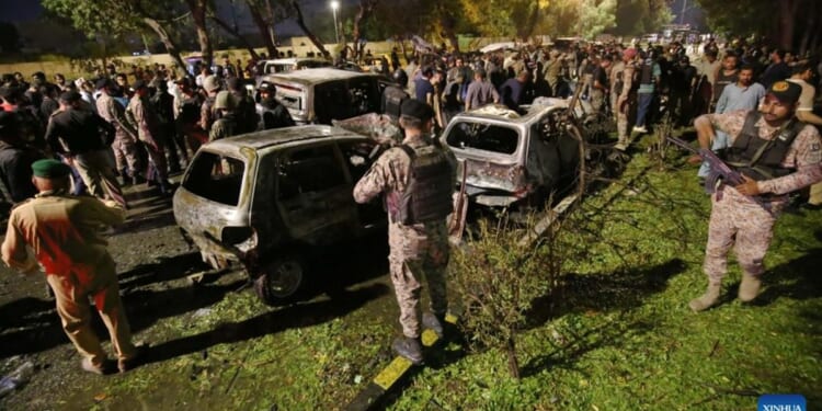 Crowd gathers around damaged vehicles at night, following an incident, with security personnel present and emergency response visible.