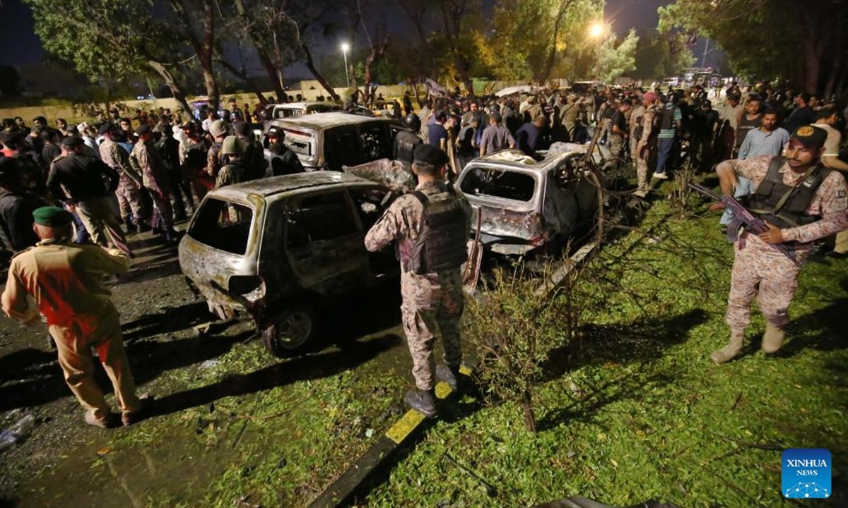 Crowd gathers around damaged vehicles at night, following an incident, with security personnel present and emergency response visible.