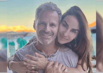 Couple smiling together outdoors with a scenic sunset background, showcasing affection and happiness in a relaxed setting.