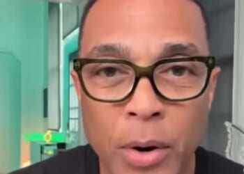 Close-up of a man with glasses speaking directly to the camera in a well-lit room with modern decor.