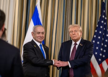 Israeli Prime Minister Benjamin Netanyahu and former U.S. President Donald Trump shake hands during a formal event, with flags of both nations in the background.