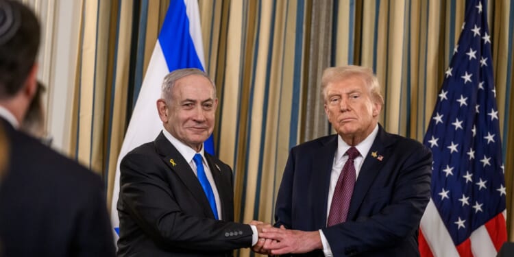 Israeli Prime Minister Benjamin Netanyahu and former U.S. President Donald Trump shake hands during a formal event, with flags of both nations in the background.