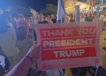 Crowd holding a sign that reads thank you President Trump during a nighttime rally or gathering.