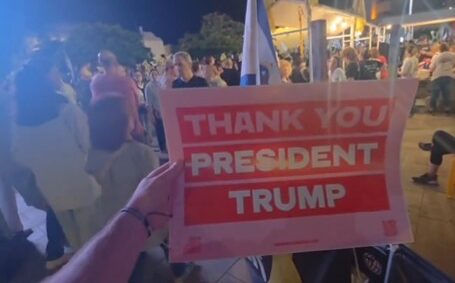 Crowd holding a sign that reads thank you President Trump during a nighttime rally or gathering.
