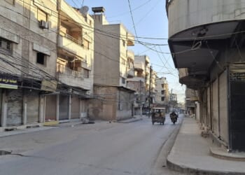 Empty street scene in an urban area with buildings, shops, and tangled overhead wires during daylight.