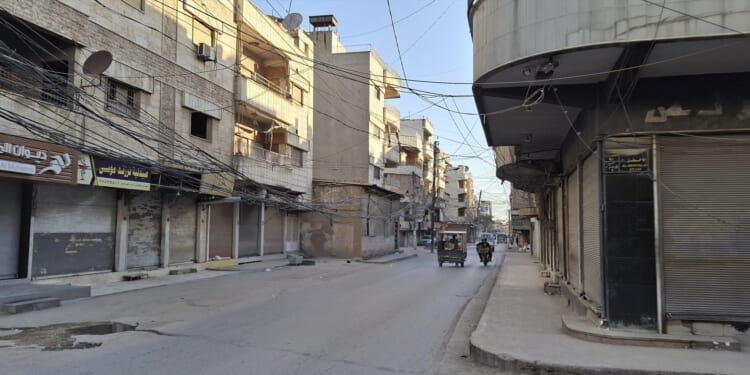 Empty street scene in an urban area with buildings, shops, and tangled overhead wires during daylight.