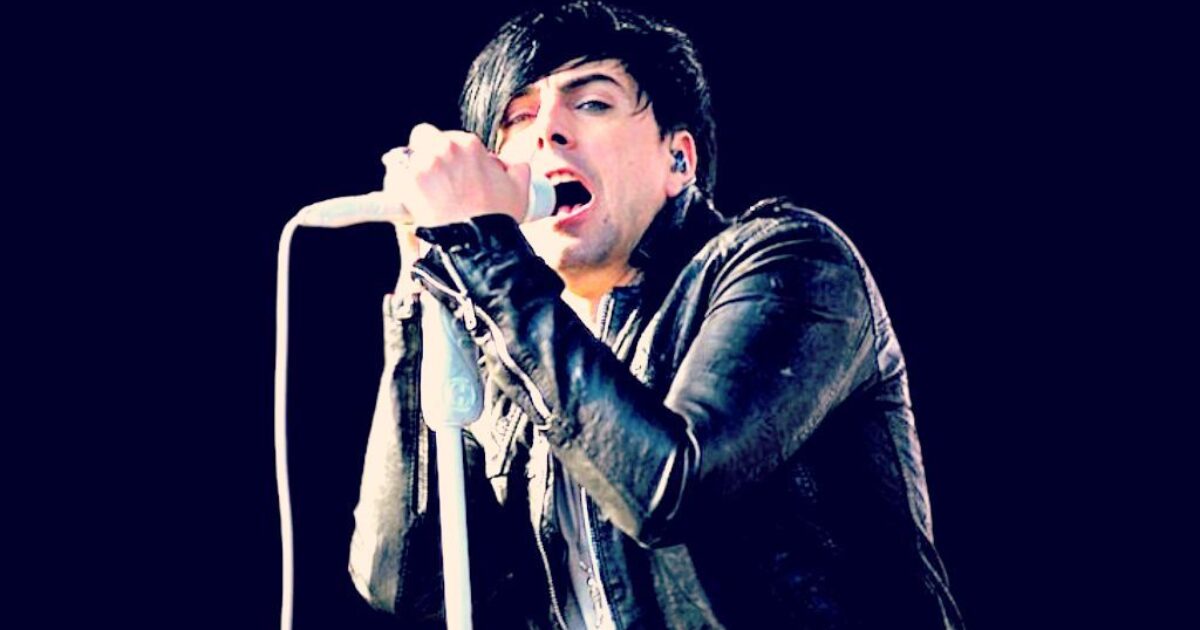 Singer performing on stage with a microphone, wearing a black leather jacket, showcasing an energetic and passionate performance against a dark background.