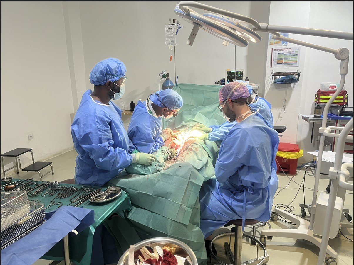 Surgeons in blue scrubs perform a surgical procedure in a well-equipped operating room, surrounded by medical instruments and equipment.