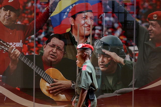 Venezuela's Presidential Honor Guard members walk past a mural with images of former President Hugo Chavez during the national recruitment campaign launched by the government of President Nicolas Maduro at the 23 de Enero neighborhood in Caracas on August 30, 2025. Hundreds of people heeded President Nicolas Maduro's call on August 29, 2025 to enlist in Venezuela's military forces to bolster ranks in the face of "imperialist aggression" from the United States. (Photo by Pedro MATTEY / AFP)