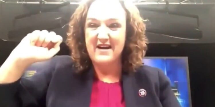 Woman in a blazer passionately speaking with a raised fist, expressing strong emotions in a broadcast studio setting.
