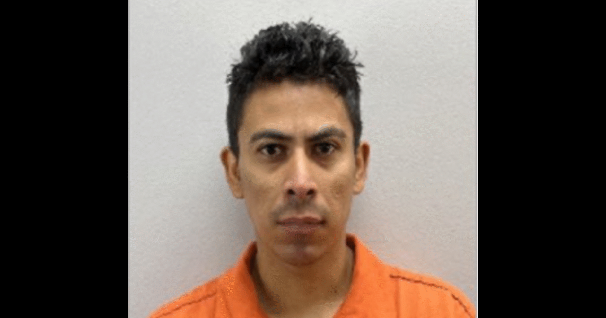 Mugshot of a man in an orange prison uniform, with short black hair and a serious expression, set against a plain background.