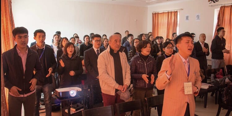 A diverse group of people engaged in a worship service, singing and expressing devotion in a bright, indoor setting.