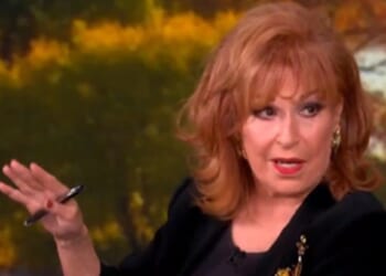 Joy Behar speaking animatedly on a talk show set, gesturing with a pen against a blurred autumn background.