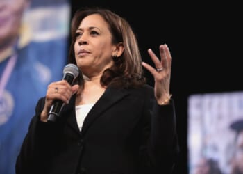 Kamala Harris speaking passionately into a microphone during a public event, emphasizing key points with hand gestures.
