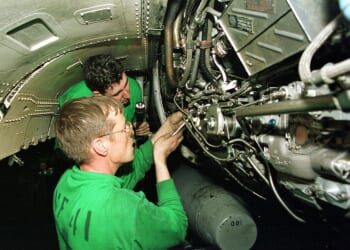 Two sailors repair a jet engine.
