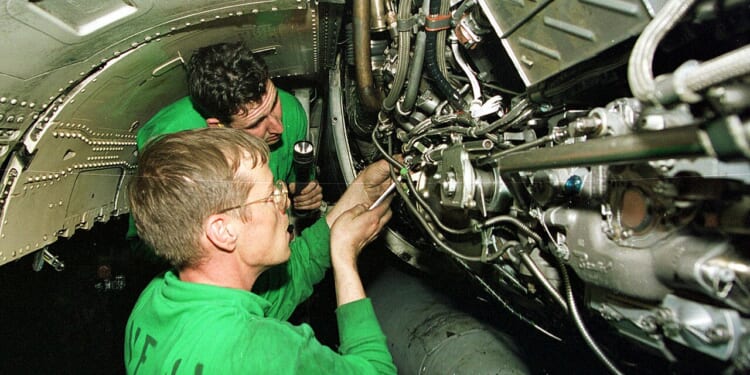 Two sailors repair a jet engine.