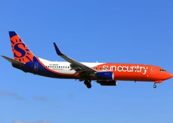 Sun Country Airlines Boeing 737-800 flying against a clear blue sky, showcasing its vibrant orange and blue livery.