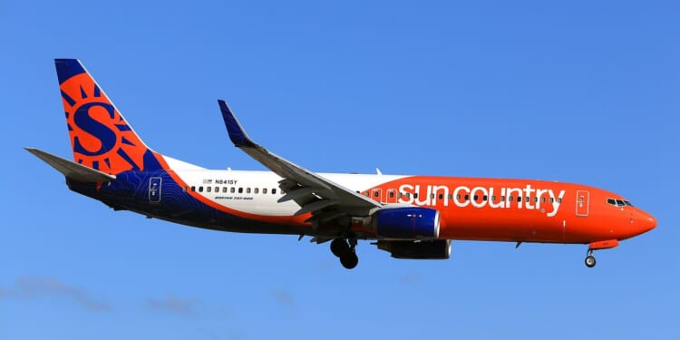 Sun Country Airlines Boeing 737-800 flying against a clear blue sky, showcasing its vibrant orange and blue livery.