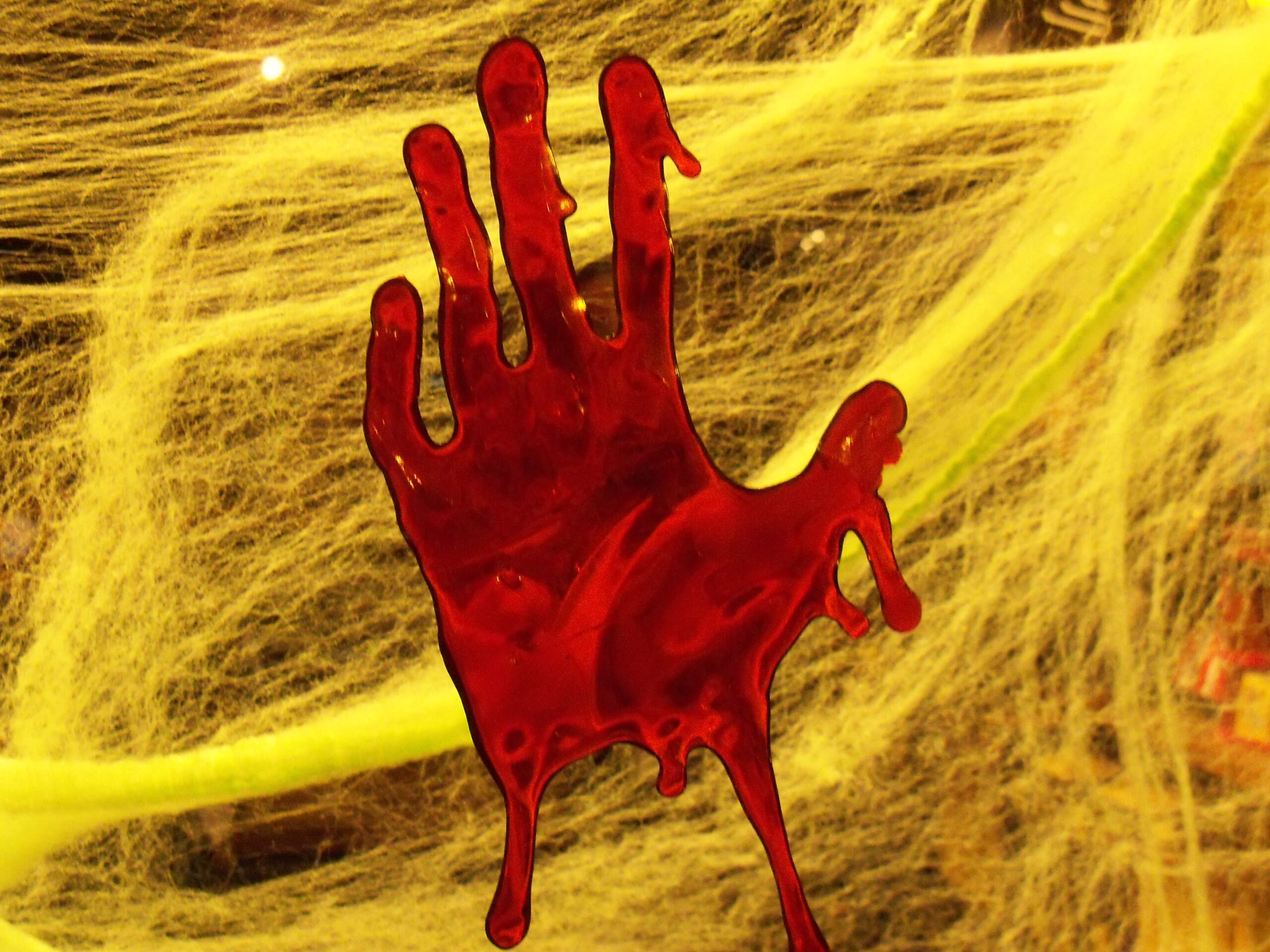 Red handprint on a yellow spider web background, creating a spooky atmosphere suitable for Halloween decorations.