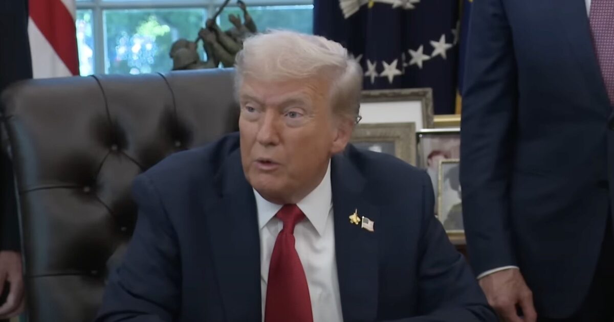 Donald Trump seated at the Resolute Desk in the Oval Office, engaging in conversation during a meeting with advisors.