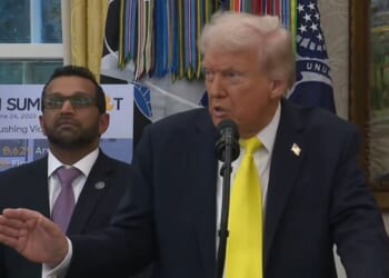 Donald Trump speaking at a podium in the Oval Office, with an official in a suit standing beside him, discussing the upcoming FBI Summit.