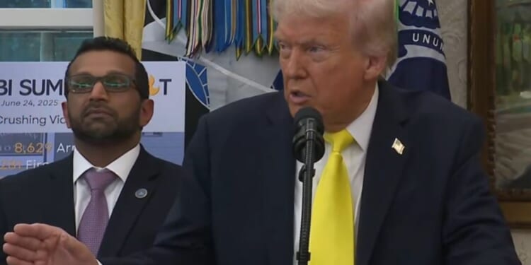 Donald Trump speaking at a podium in the Oval Office, with an official in a suit standing beside him, discussing the upcoming FBI Summit.