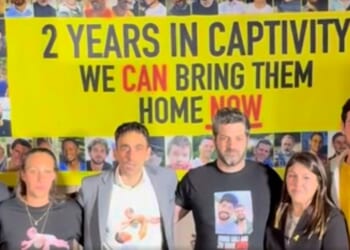 Group of activists standing in front of a banner advocating for the return of individuals held in captivity for two years, emphasizing urgency and support.