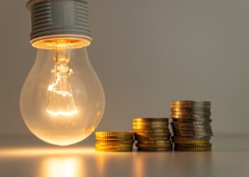 Lighbulb next to gold coins, symbolizing AI's impact on electricity prices