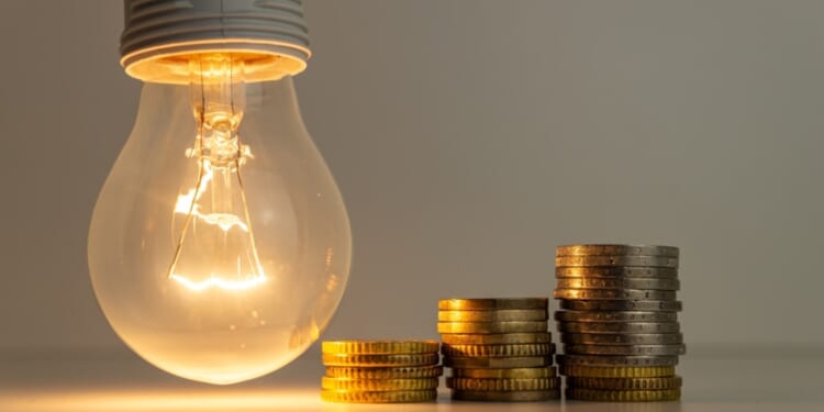 Lighbulb next to gold coins, symbolizing AI's impact on electricity prices