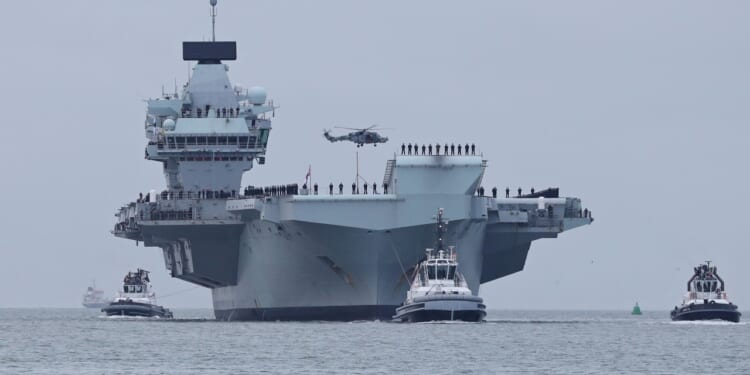 A Royal Navy Wildcat helicopter makes a low pass over the aircraft carrier HMS QUEEN ELIZABETH as the ship returns home to the Naval Base after 7 months away