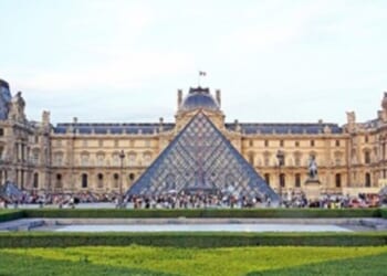 Louvre Museum with iconic glass pyramid, surrounded by historic architecture and lush gardens, attracting numerous visitors in Paris, France.