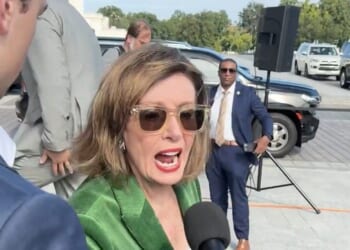 Nancy Pelosi speaking to the media while surrounded by security and vehicles, showcasing her engagement in a public event.